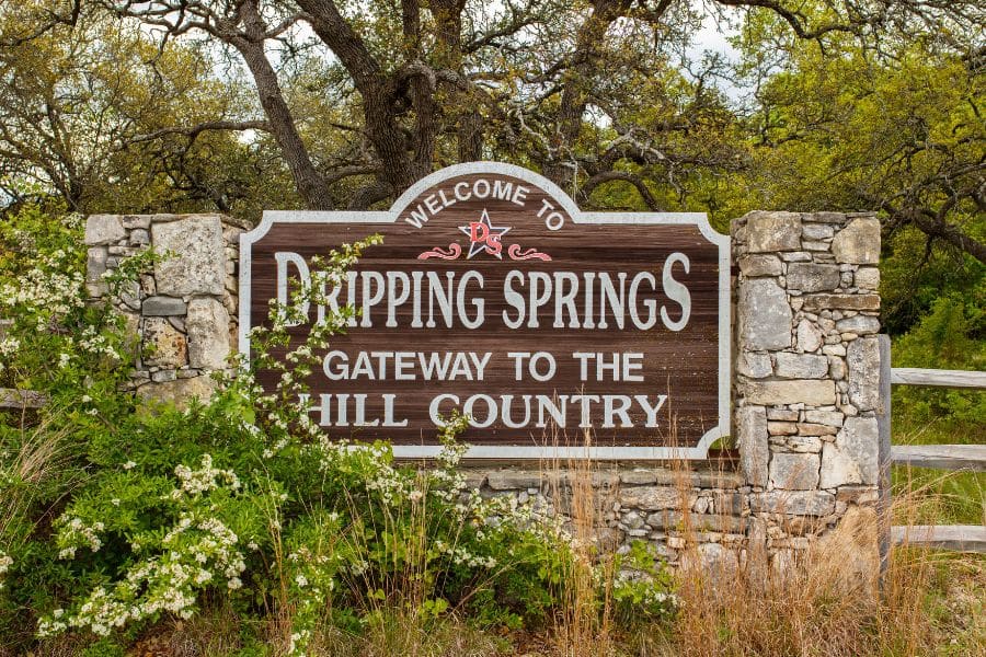 Welcome to Dripping Springs - Gateway to the Hill Country roadside sign surrounded by wildflowers and oak trees