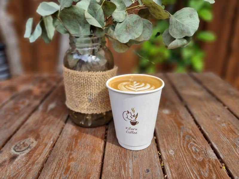 A Kifaru Coffee branded cup with latte art, alongside a hessian-wrapped glass jar and green foliage.